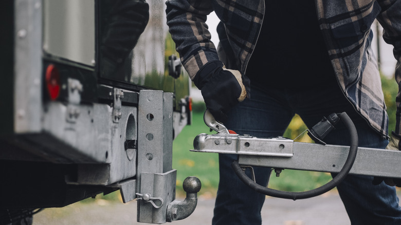 A man attempting to attach a camper trailer to a vehicle's towing hitch